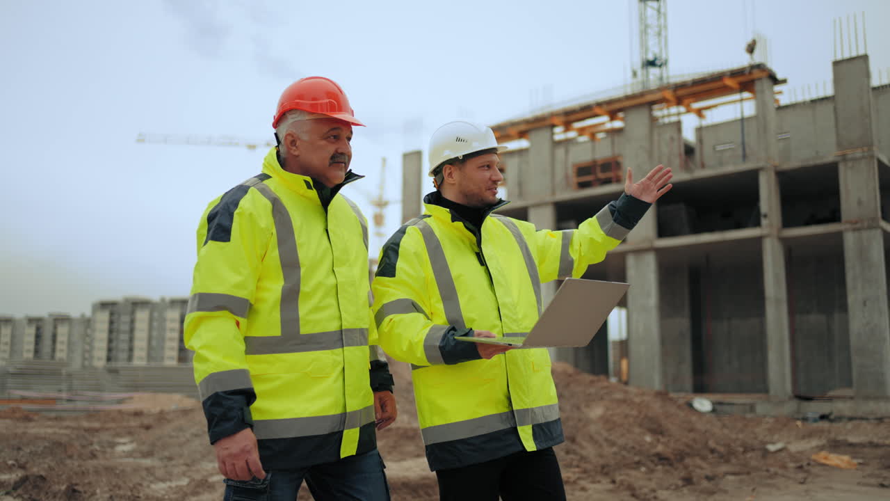 dos capataces en cascos duros y uniforme están caminando en el área de construcción de un complejo residencial moderno