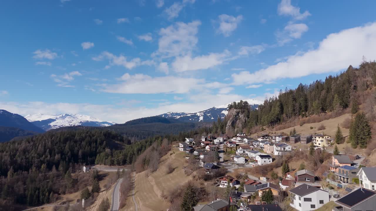 Trin, switzerland, showcasing homes nestled between forested hills and snow-capped mountains, aerial view