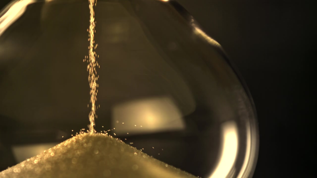 Close-up of Golden Sand Falling in an Hourglass on a Dark Background