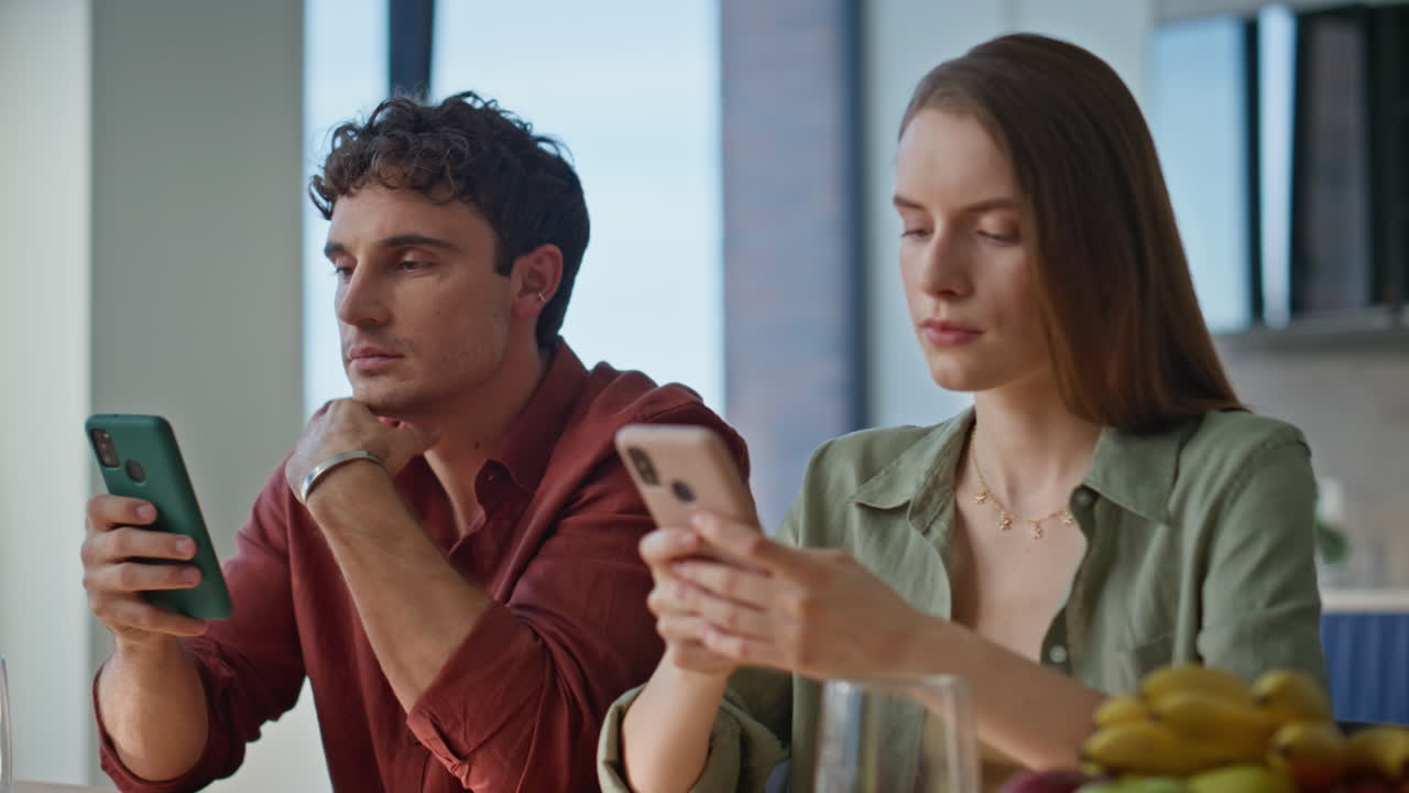 Young pair focused mobile phones at domestic breakfast in apartment closeup