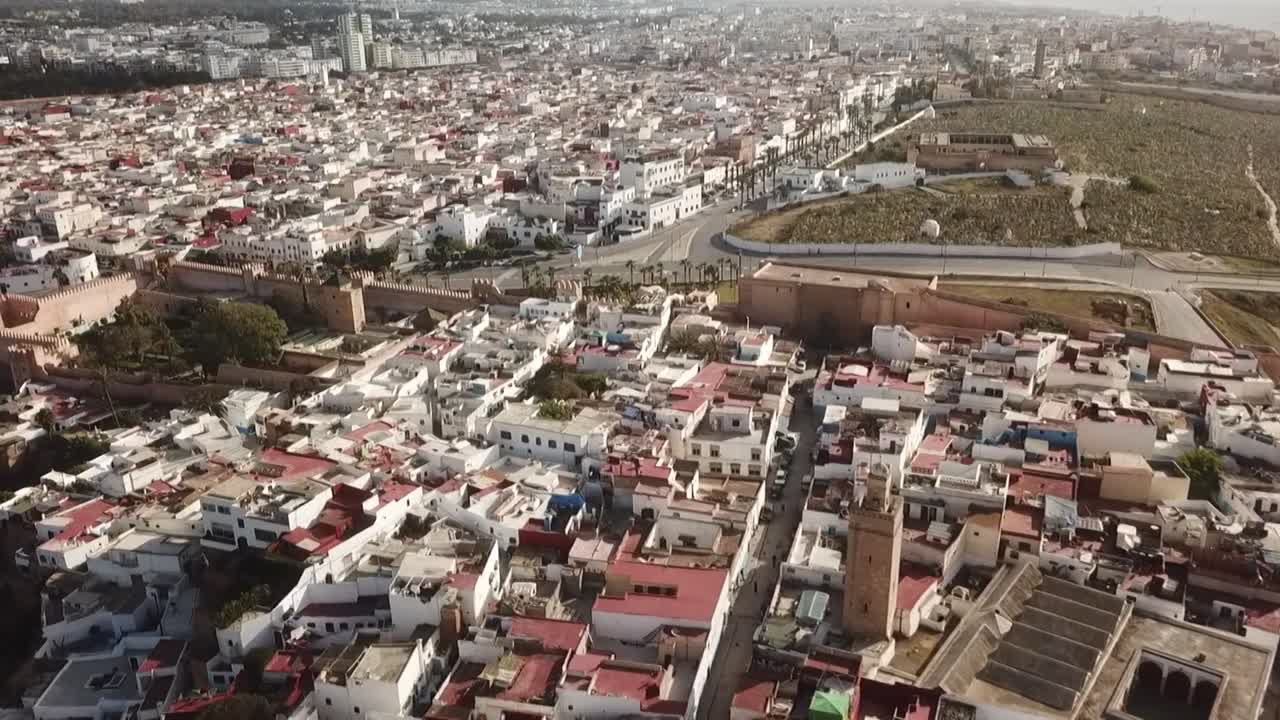 Detailed drone shot of Rabat's old medina. Captures the dense white buildings, mosque minarets, historic ramparts, and the transition to the open urban landscape outside the walls