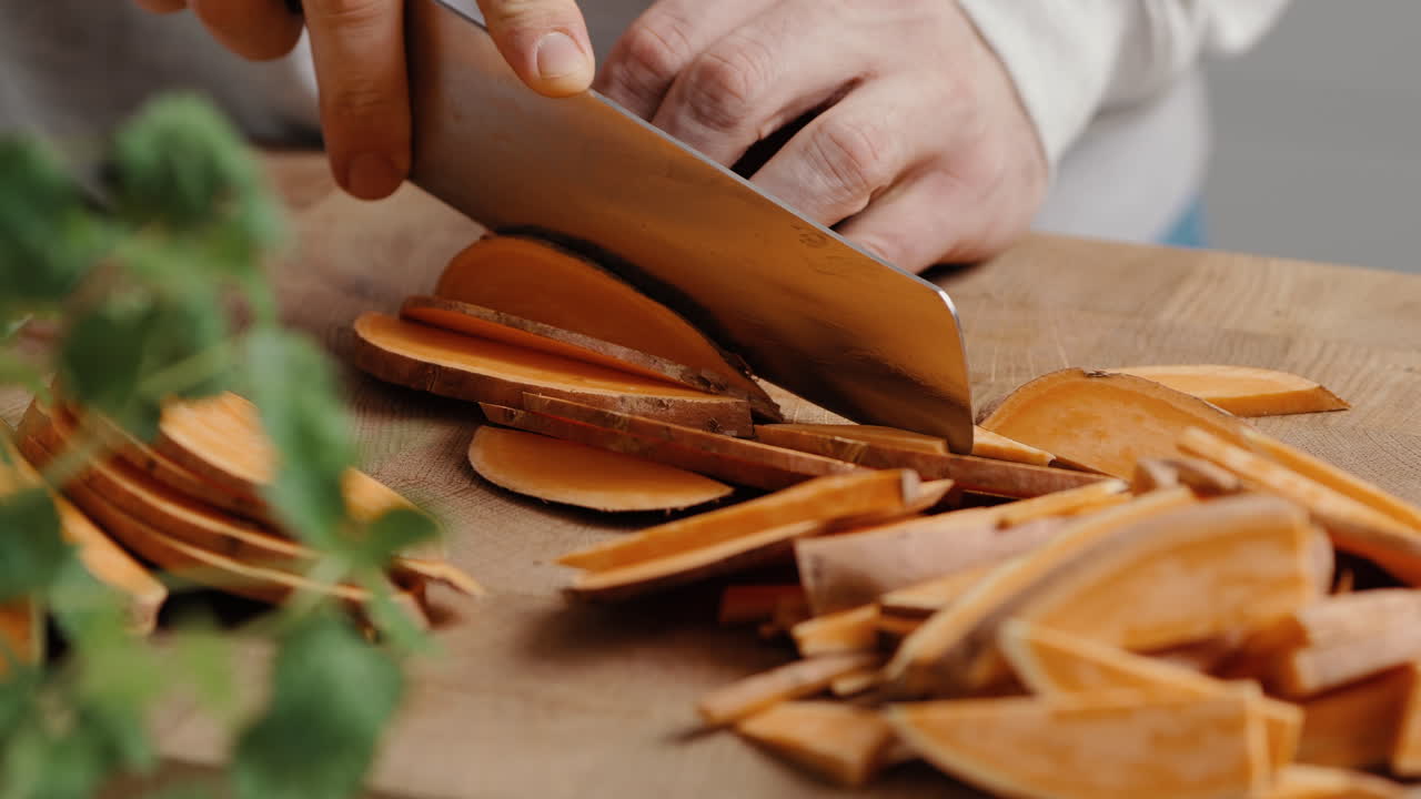 Male chef sliceing sweet potato in thin slices in the kitchen on a wooden cutting board in the kitchen