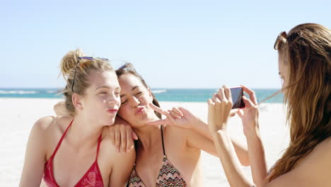 Three-teenage-girl-friends-taking-photo-on-beach-wearing-colorful-bikini-sharing-vacation-photo
