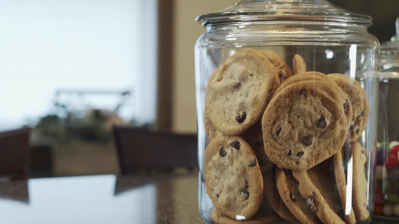 Rack focus shot of modern kitchen across table to jar of chocolate chip cookies