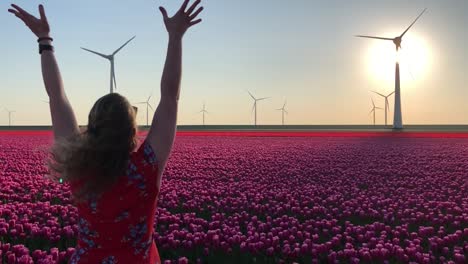 girl in field of tulips and wind turbines throwing flowers in air