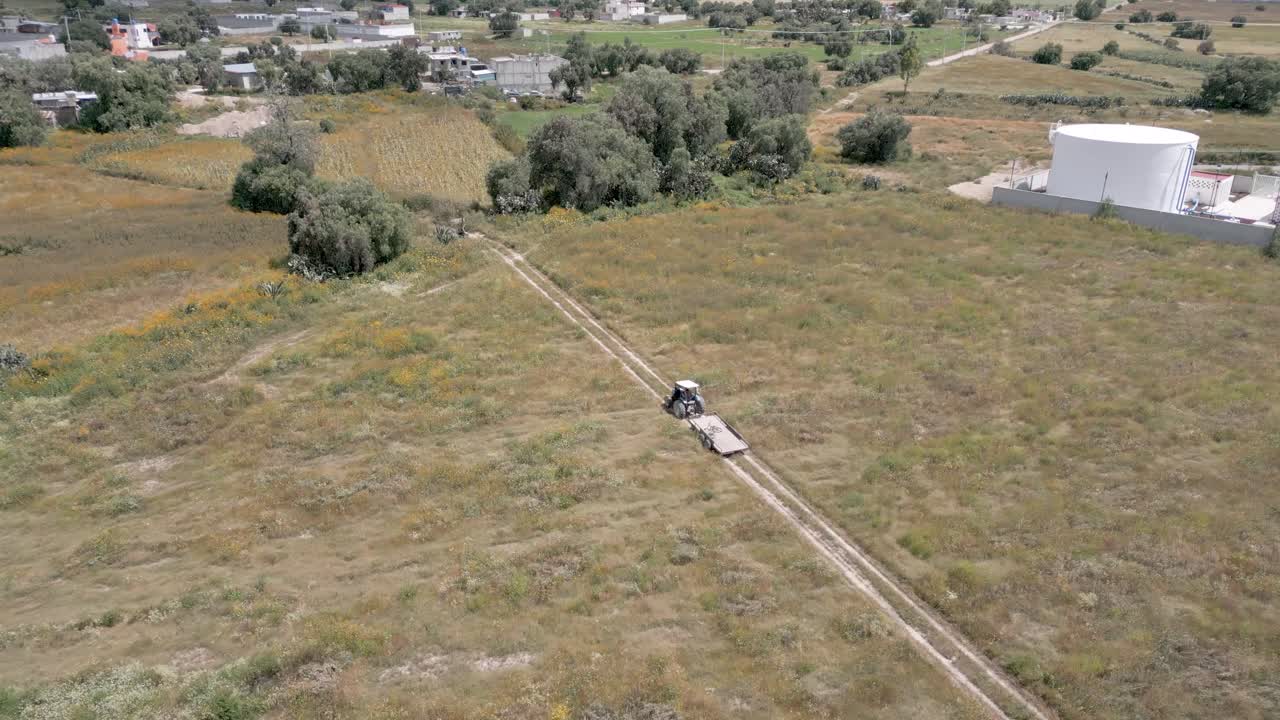 Drone Aerial Tracking Shot of Tractor Driving Through Rural Farmland Beside New Housing Development in Mexico – Sunny 4K