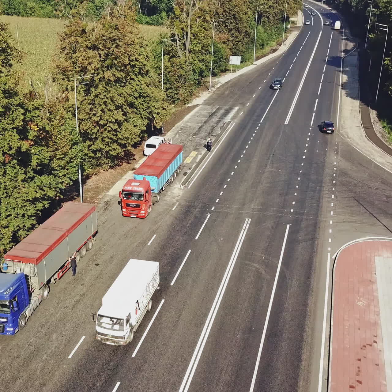 Patching repair of a piece of road outside the city on the background of two standing trucks and the movement of cars near the intersection. Aerial view.
