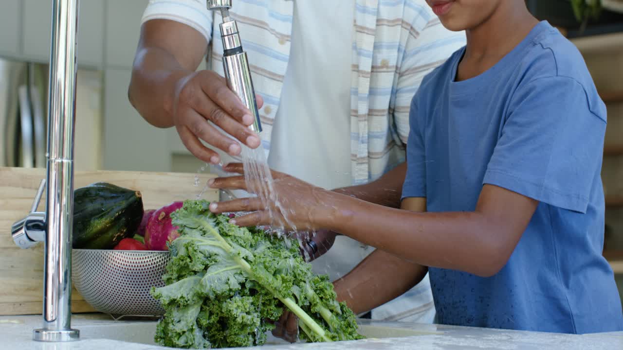 Père afro-américain et son fils adolescent ouvrant le robinet de l'évier de la cuisine pour rincer des légumes verts pour une salade