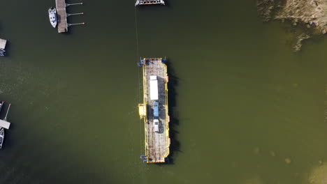 Aerial-top-down,-drone-shot-of-a-cable-ferry,-arriving-at-a-dock,-in-the-archipelago-of-Porvoo,-sunny,-spring-day,-in-Uusimaa,-Finland