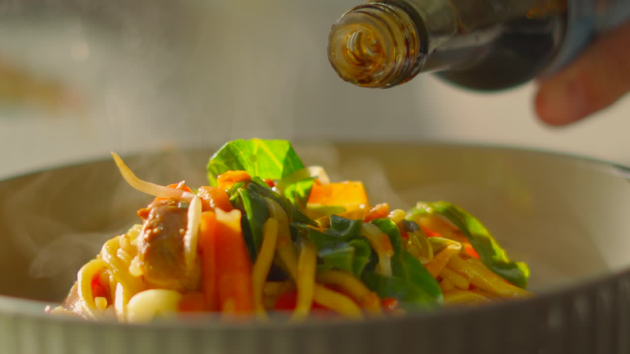 Soy Sauce Being Poured on Freshly Cooked Oriental Style Chicken Stir Fry with Crunchy Vegetables and Noodles. High Details on Droplets as Food is Seasoned.