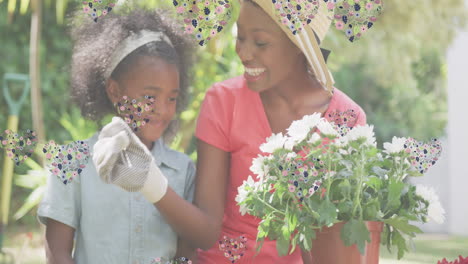 animation of hearts over smiling african american mother and daughter gardening plants