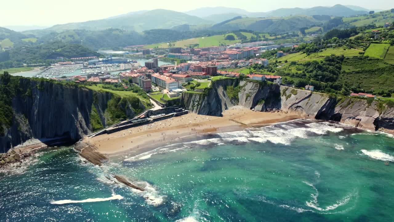 Aerial view of a beach with cliffs, mountains, and a town in the background