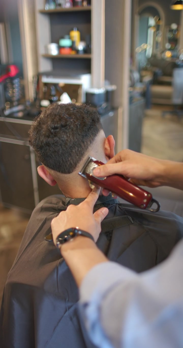 Video verticale: Barbiere con tagliacapelli che rifinisce la sfumatura sulla nuca in un barbershop