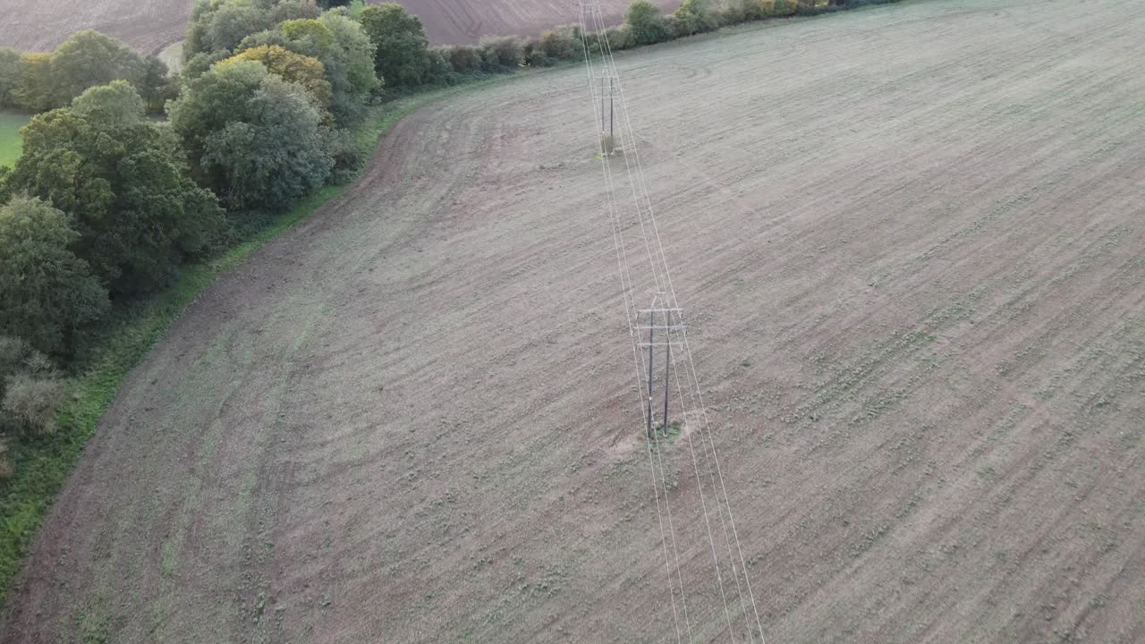 líneas de energía eléctrica en tierras de cultivo uk drone vuela a lo largo de la ruta de las líneas que pasan a través de los árboles a fines del verano