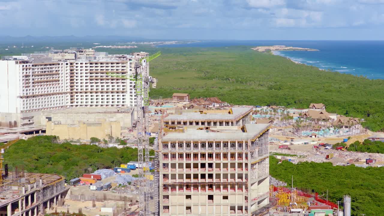 Vista aerea di un grande complesso turistico alberghiero in costruzione a Punta Cana, Repubblica Dominicana, con gru a torre e strutture in crescita su rigogliosi paesaggi tropicali. Rapida crescita del turismo sull'isola caraibica