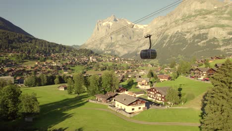 dolly de lado de derecha a izquierda con vistas de una cabina que desciende en el sistema de coches tricable eiger express frente al pueblo de grindelwald y el monte wetterhorn