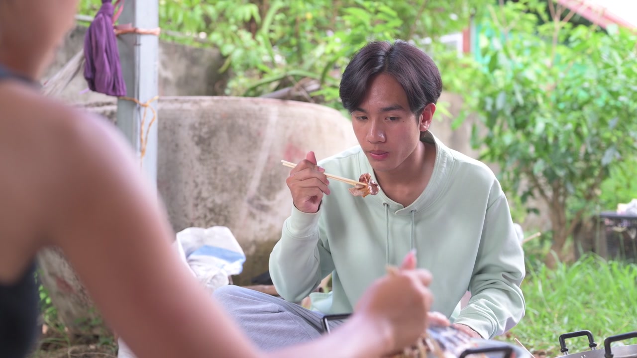ชายหนุ่มชาวไทยผู้มีความสุขจากภาคอีสานกำลังทำหมูกระทะด้วยตะเกียบ