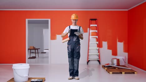 full body of asian man painter wearing safety helmet using a tablet while standing with painting wall in room