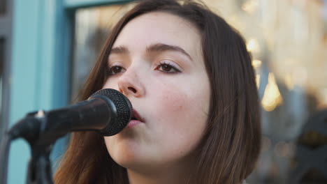 female musician busking singing into microphone outdoors in street