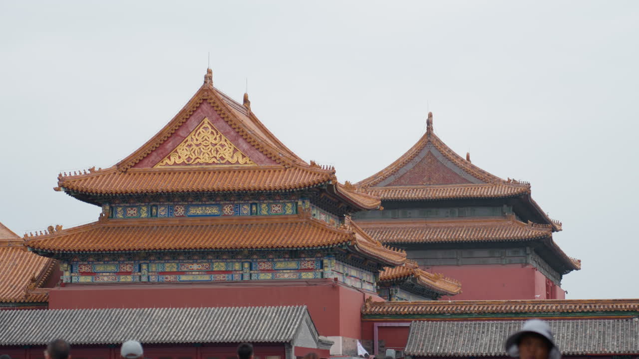 Dächer der Verbotenen Stadt mit asiatischen Touristen, verzierte goldene Ziegel und bewölkter Himmel, Reiseführer führt Gruppe, während Fotograf Dachüberstände einrahmt, Rucksacktourist pausiert für eine Aufnahme nahe einem Denkmal, historisches Tor und detaillierte Architektur.