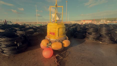 Una-Orgullosa-Boya-De-Navegación-Amarilla-Se-Alza-En-El-Muelle-De-Un-Pueblo-Pesquero-Costero-Español,-Sirviendo-Como-Símbolo-De-Seguridad-Marítima-Y-Orientación-En-Medio-De-Las-Bulliciosas-Actividades-Portuarias.