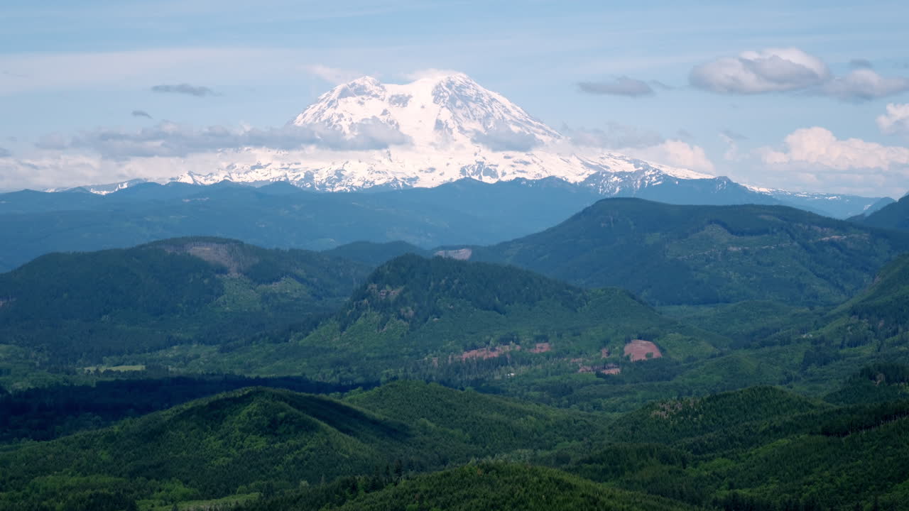 Il Monte Rainier con la cima innevata si erge sopra dolci colline verdi e crinali boscosi sotto un cielo parzialmente nuvoloso nello Stato di Washington
