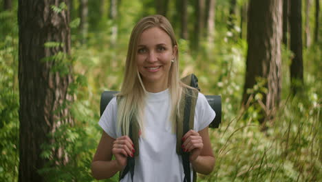 portrait of a young woman traveler in the sun looking directly into the camera and smiling flirting traveler with a backpack in the park and in the woods in slow motion