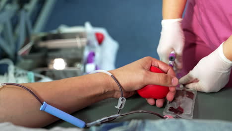 male donor's hand with the iv drip attached. medic fills the test tubes with blood. close up.