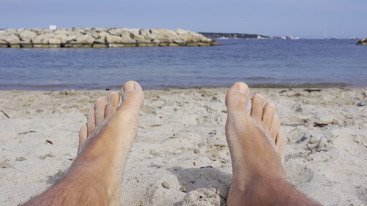Close up of a man's wet and sandy feet on a beach with a view of the sea