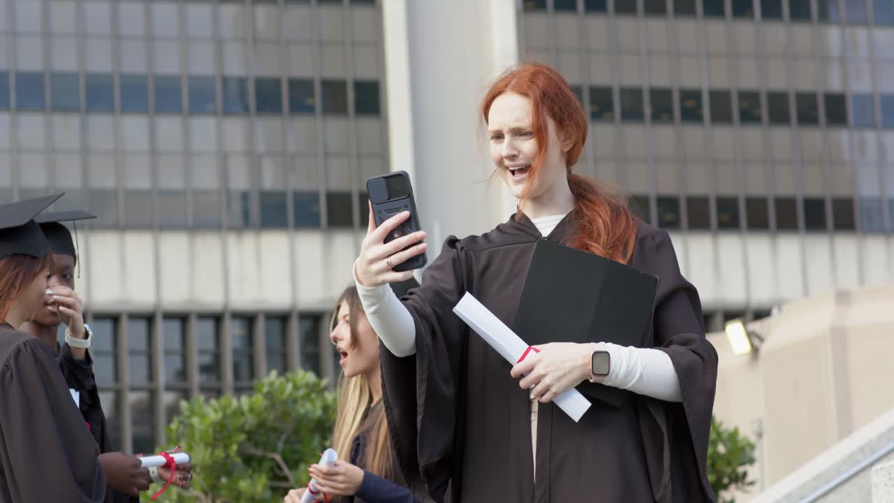 Diverse laureate che alzano lo smartphone durante un selfie di laurea sui gradini, ridendo e sistemandosi il tocco.
