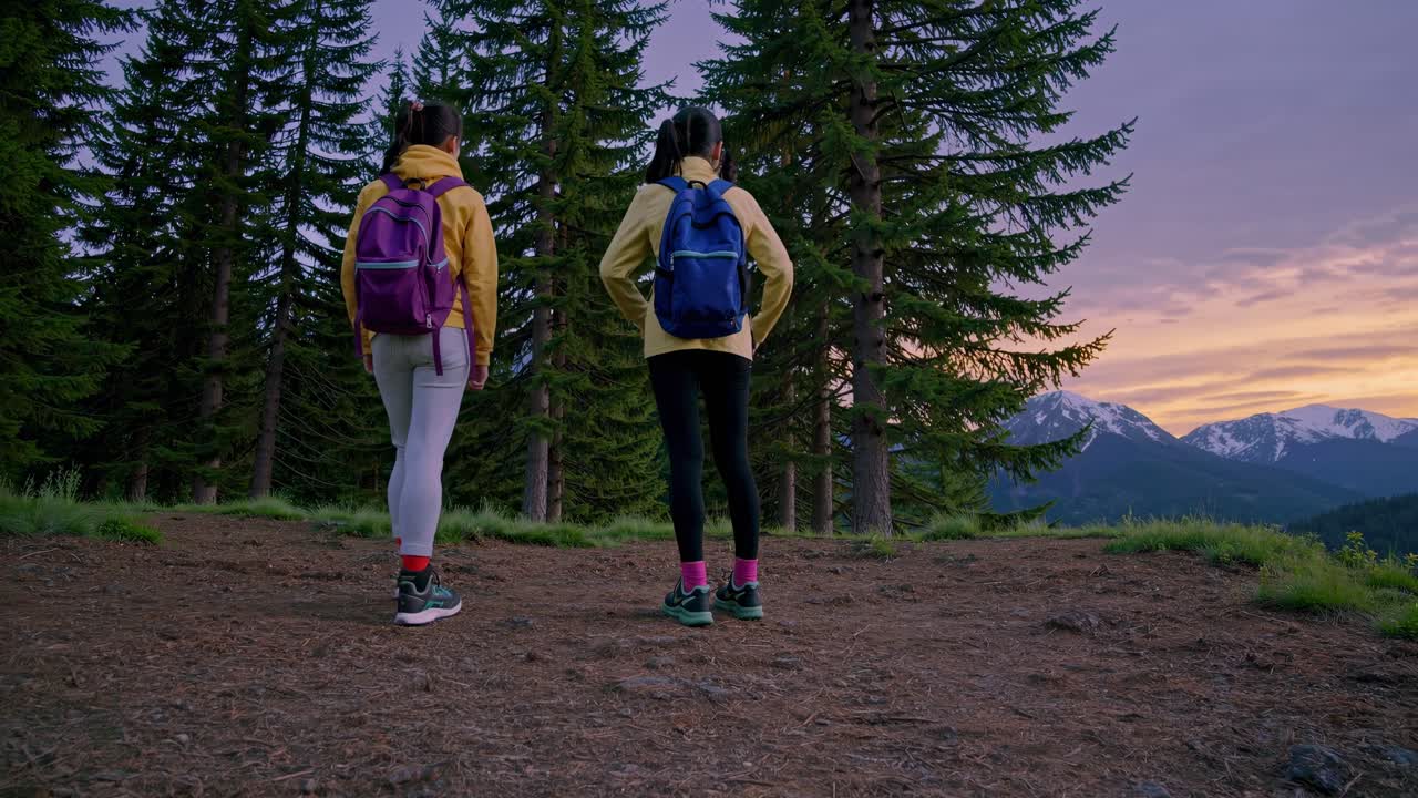 Two hikers with backpacks savoring a breathtaking mountain view at sunset, standing atop a hill in a serene forest, surrounded by tranquil trees and vibrant colors in the sky