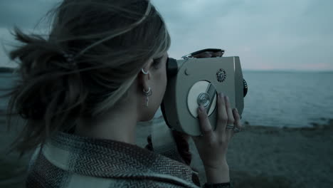 mujer grabando un video con una cámara vintage en la orilla del lago