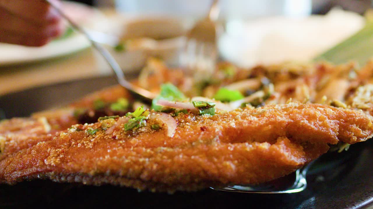 Close-up of crispy fried fish garnished with herbs, served in warm restaurant lighting, handheld camera