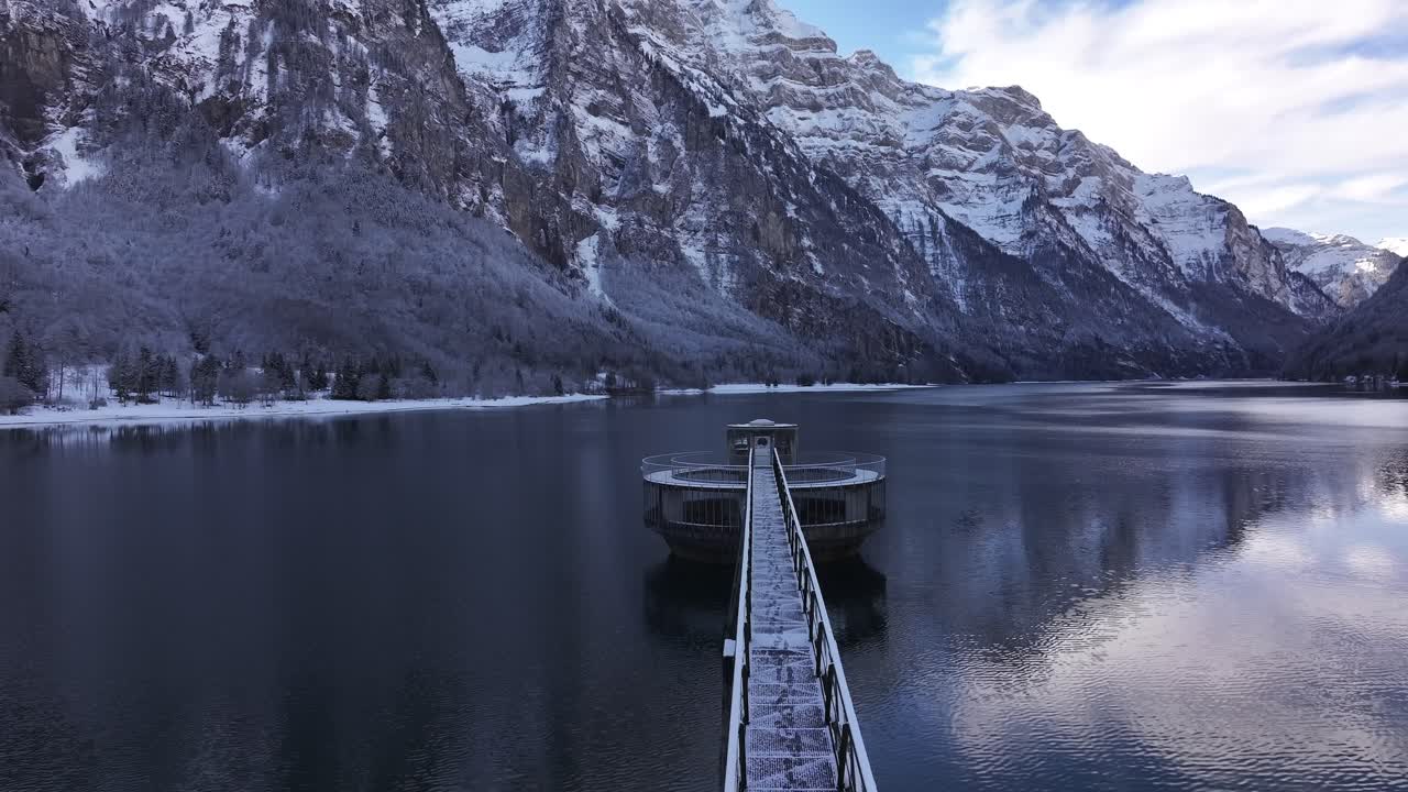 Snow dusted pier extending into Klöntalersee with Vorderglärnisch peaks in Glarus, Switzerland