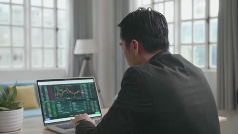 un hombre de negocios asiático con traje de negocios mirando el gráfico de acciones en la computadora mientras trabaja en casa.