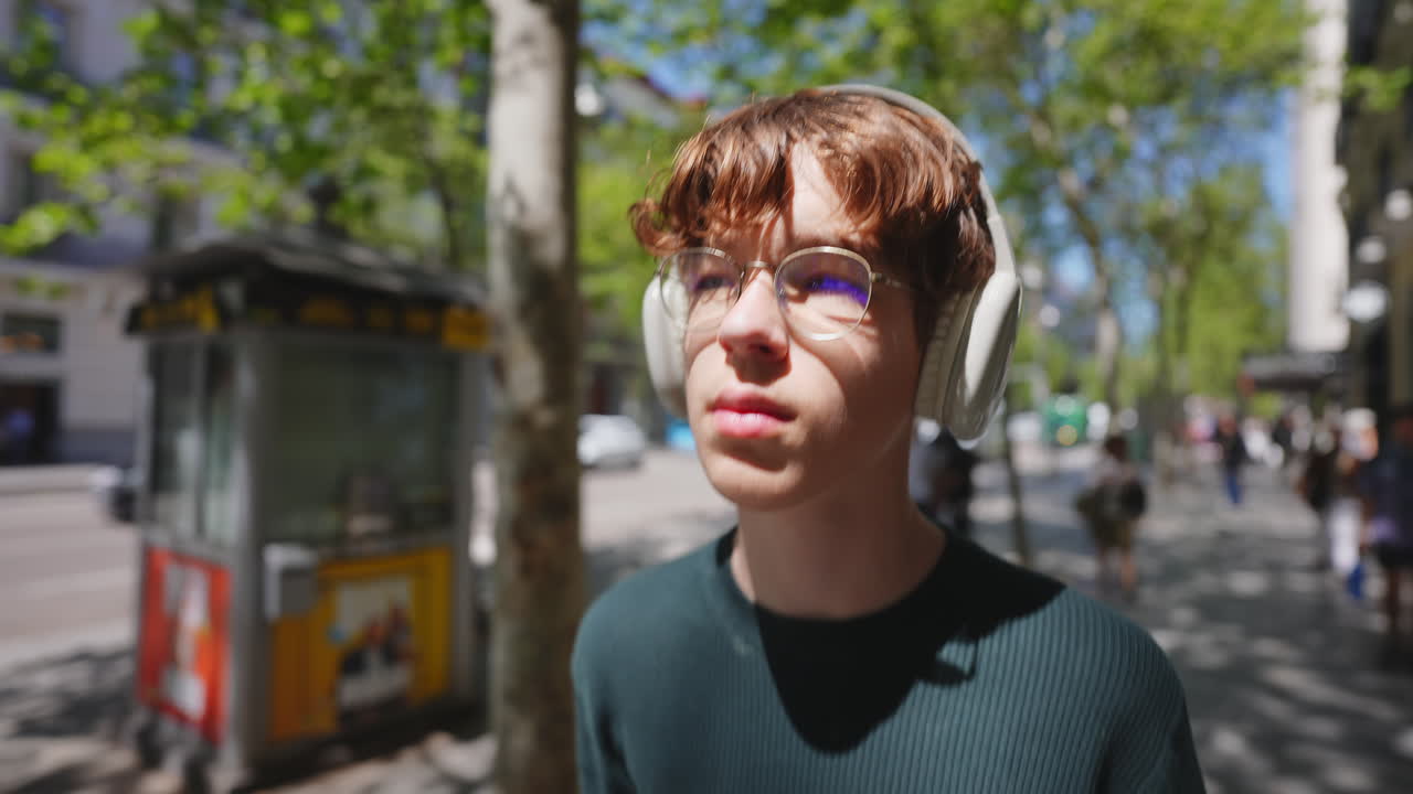 Joven con auriculares caminando por una calle soleada de la ciudad