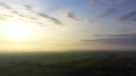 Brumoso-Amanecer-Sobre-El-Paisaje-Rural-Con-Turbinas-De-Viento-En-El-Fondo