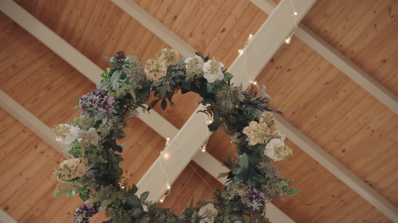 Medium shot of a floral wedding wreath gently moving in the wind while the camera spins slowly beneath it