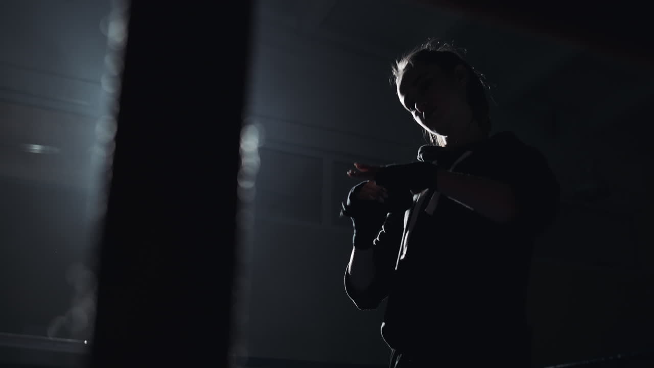 Silhouette of a Woman Preparing for Boxing Training in a Dark Gym
