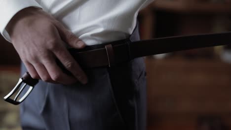 handsome groom fixes his belt with pants. wedding morning. businessman