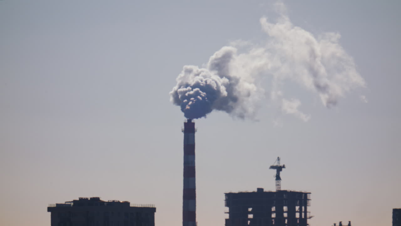Ciminiera industriale che rilascia fumo denso nel cielo sopra un cantiere edile cittadino.
