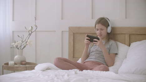 children and internet games little girl is playing by smartphone sitting in bedroom internet addiction pastime at home during self-isolation