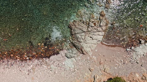 Stunning-Pebble-And-Rocky-Beach-With-Crystal-Clear-Tropical-Water-On-A-Sunny-Day-In-Sardinia,-Italy---aerial-drone-shot,-top-down