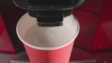coffee machine dispensing water into red paper cup with milk foam, creating soft texture. ideal for cafe scenes, drink preparation, coffee machines, and milk based beverages