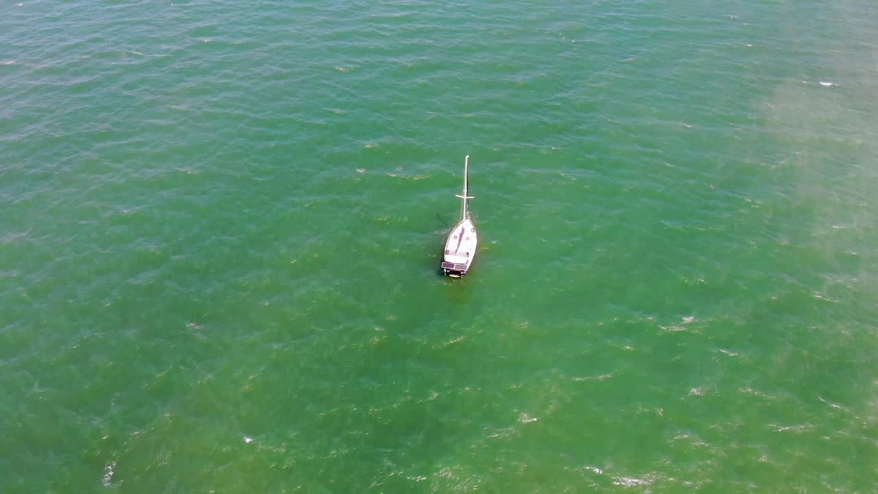 un pequeño velero que circula desde arriba mientras flota a través de pequeñas ondas de agua verde esmeralda y azul demin en un hermoso día soleado y cálido