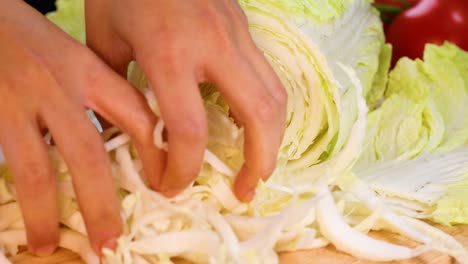 manos triturando repollo chino en una tabla de cortar