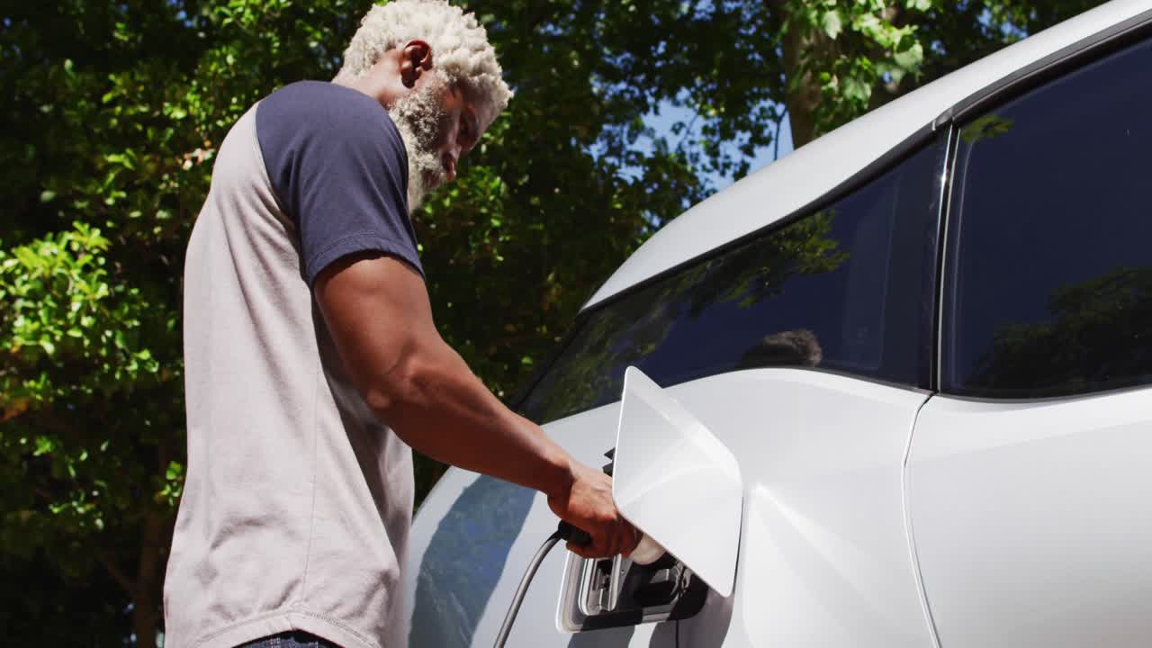 hombre mayor afroamericano cargando un coche eléctrico en un día soleado