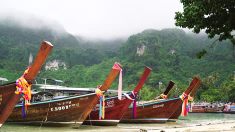 Traditional-Thai-long-tail-boats-moored-on-beach,-lush-jungle-mountain-landscape