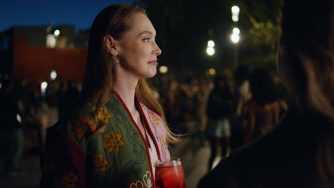woman holding cocktail talking with friends at night city party outdoors closeup