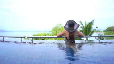 a young woman with her back to the camera leans along the swimming pool railing as she looks out of the oceanview